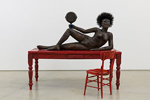 Alison Saar / 
Set to Simmer, 2019 / 
wood, ceiling tin, enamel paint ceiling tin wire, found table, chair, and skillet with texts by Dionne Brand / 
Table and figure: 65 x 72 x 36 in. (165.1 x 182.9 x 91.4 cm) / Chair: 38 x 16 x 16 in. (96.5 x 40.6 x 40.6 cm)