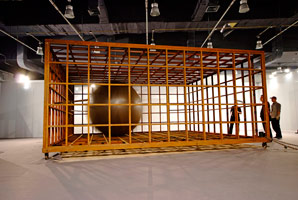 Sui Jianguo / 
Limited Moving, 2010 / 
Steel and electric machinery / 
 / 
Viewers are confronted by oversized mobile steel spheres that /  are activated, yet confined within industrial steel walls, cages /  or the gallery space itself. These massive globes are set into /  motion against their enclosures, producing a jarring collision /  of metal, or a rolling, physical threat.  