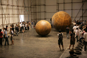 Sui Jianguo / 
Motion and Tension, 2009 / 
Steel structure and electrical machinery, iron balls / 
Height 98.43 in. (250 cm) / 
 / 
Viewers are confronted by oversized mobile steel spheres that /  are activated, yet confined within industrial steel walls, cages /  or the gallery space itself. These massive globes are set into /  motion against their enclosures, producing a jarring collision /  of metal, or a rolling, physical threat.  